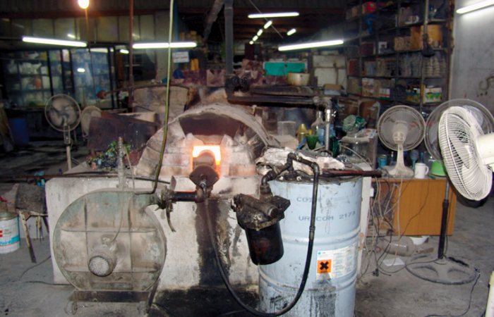 1re étape : Régler le four. Le feu est alimenté au moyen d’huile recyclée. Au fond de l’arrière-boutique, des réservoirs stockent l’huile et rejoignent l’intérieur du four par des tuyaux. Avant de commencer à travailler, il faut préchauffer le four afin qu’il atteigne la température adéquate : 1 400 degrés Celsius 