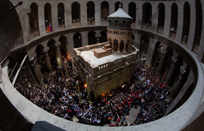 Le Feu ayant jailli du Tombeau est distribué à la foule par les deux ouvertures latérales de l’édicule, tandis que le patriarche grec-orthodoxe sort en bénissant la foule des deux cierges qu’il brandit ©MAB/TSM